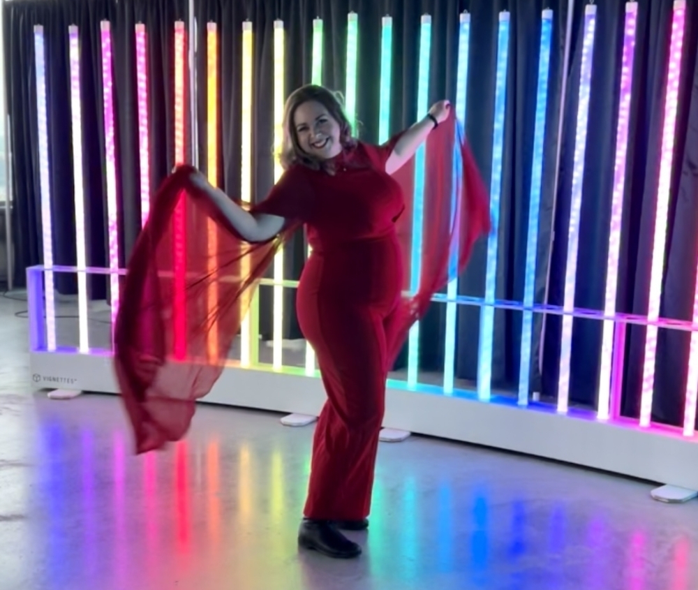 Photo of a young woman in a red dress standing in front of a light installation featuring tube lights of various colours