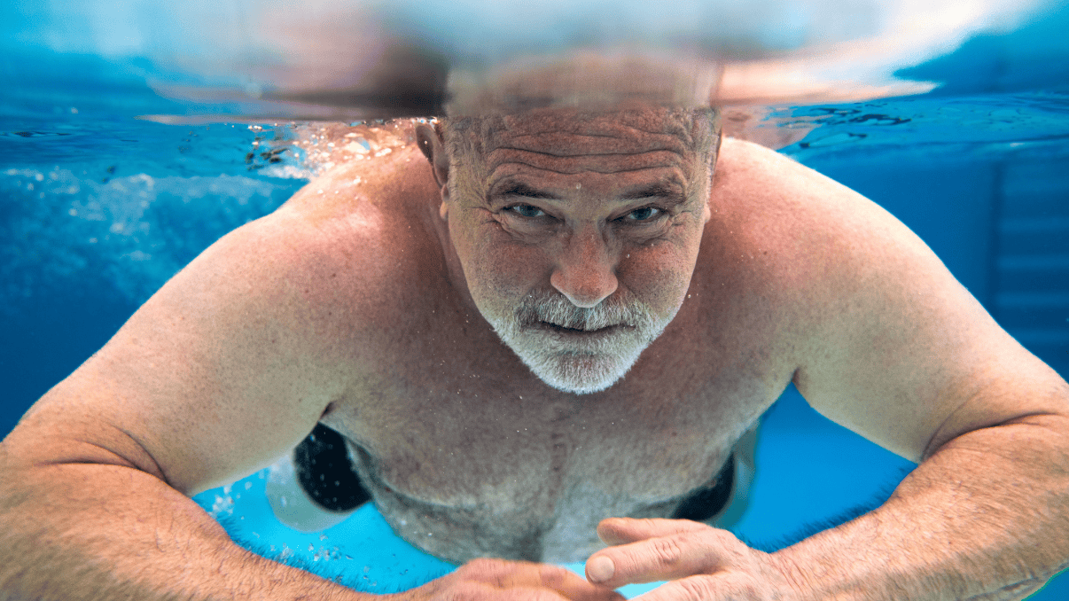An elderly man swimming underwater, showcasing resilience and recovery.
