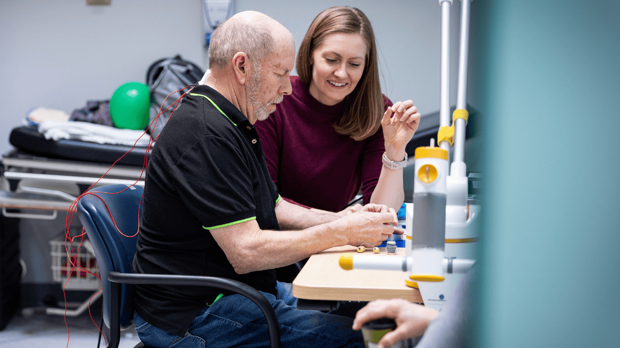 Elderly man undergoing spinal cord stimulation therapy with a caregiver in a clinical setting.