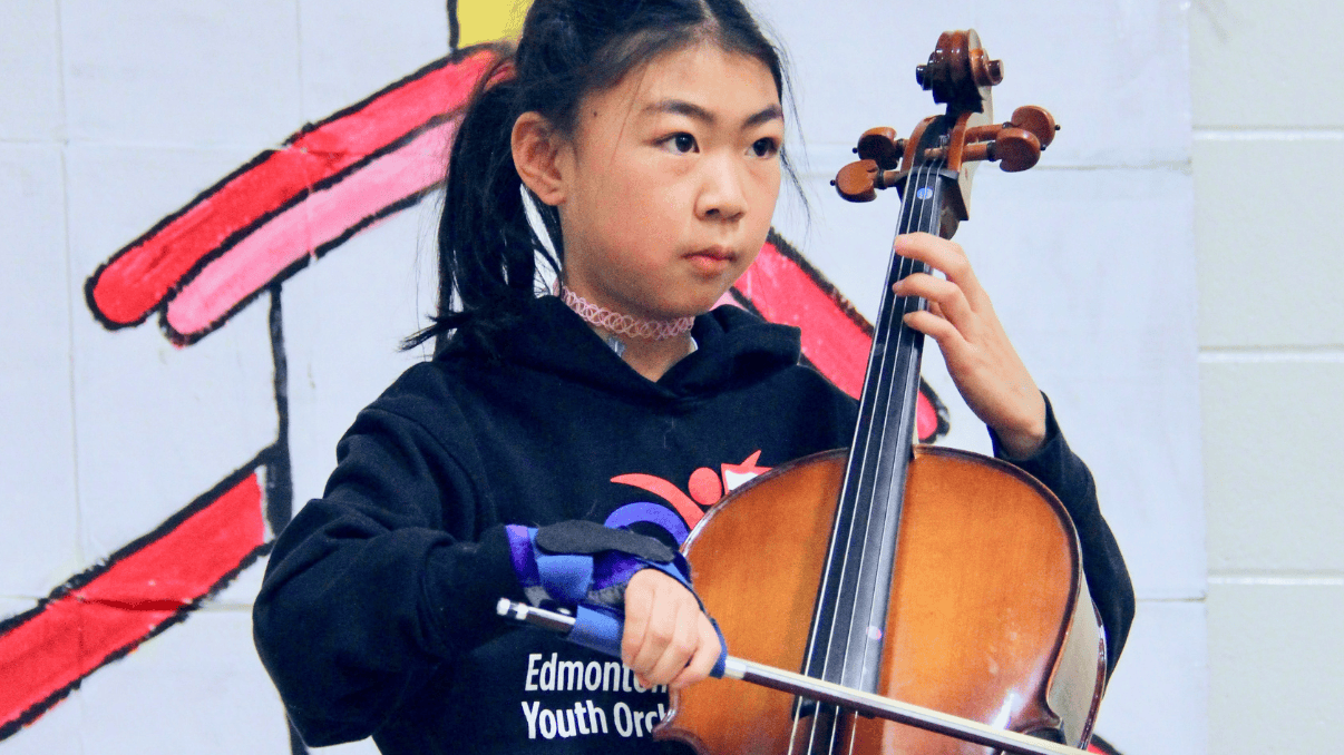 Young girl playing cello during a music therapy session at Glenrose Hospital.