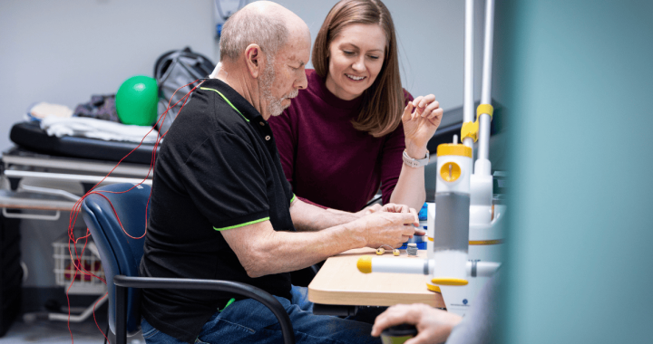 Elderly man undergoing spinal cord stimulation therapy with a caregiver in a clinical setting.