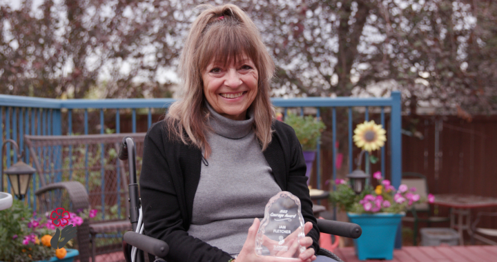 Photo of a woman sitting outside, holding an award