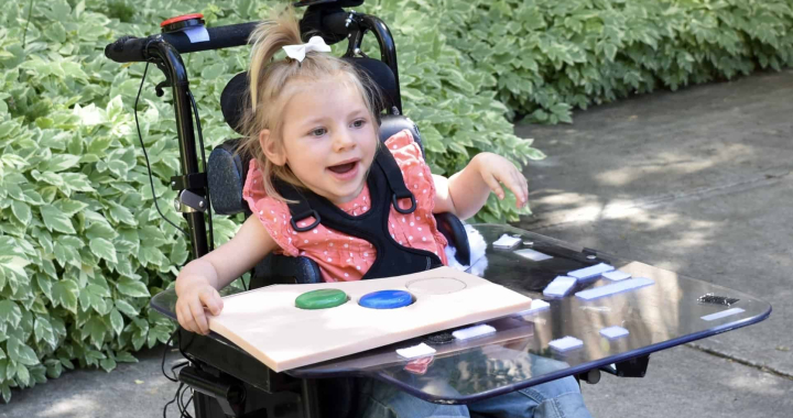 Patient Avery in her power mobility chair outside smiling.