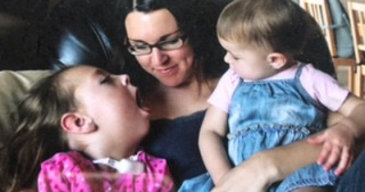 Photo of a mom with two young girls in her lap, sitting on a chair